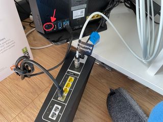 A Virgin Media Hub with a black Ethernet cable coming out of one of the yellow LAN ports. The other end of the cable is plugged into the blue WAN port of the ASUS router.